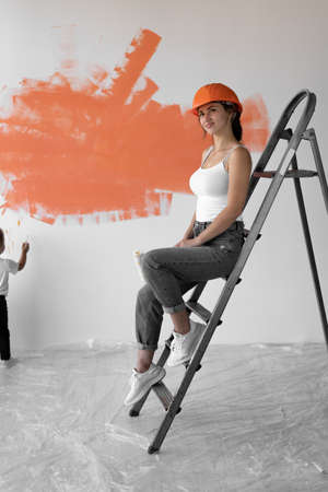 young woman sits on the stairs an orange hard hat on her head. Home renovation concept.の写真素材