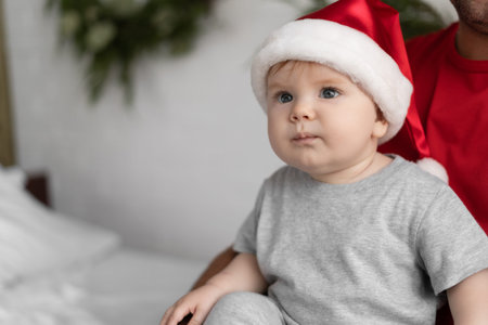 close up portrait newborn baby wearing Santa Claus hat sits on the bed. Copy space