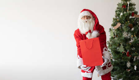 Santa Claus stands near the Christmas tree holding a large shopping bag. Baner. copy spaceの写真素材