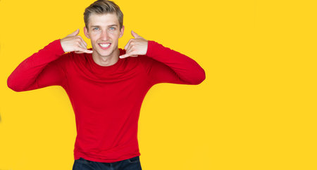 young man of European appearance on a yellow background. raises two hands up simulating a phone...