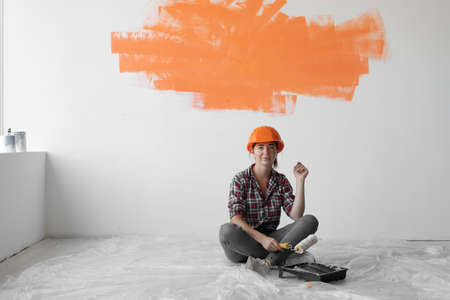 happy woman sits on the floor with orange spot on the wall. copy space. home renovation conceptの写真素材