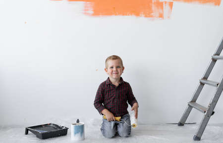 A young boy with a smile sits in a room near the stairs. Holds a paint brush in his hands. Home renovation concept.の写真素材
