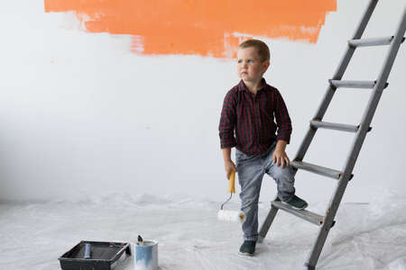 A young boy with a serious look stands in a room near the stairs. Holds a paint brush in his hands.の写真素材