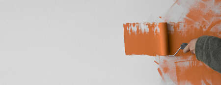 Painting the apartment, renovation with orange paint. Baner. closeup male hand paints the wallの写真素材
