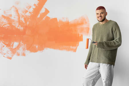 a young man of European appearance stands near the wall. Holds a paint roller. Home renovation conceptの写真素材