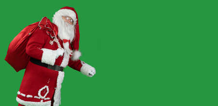 santa claus on green with a big red bag goes and looks into the camera. Baner. Copy space. Christmas and New Year conceptの写真素材