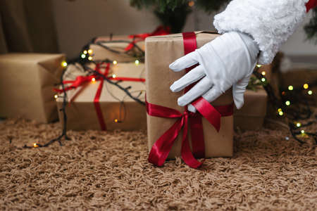 Santa claus puts a box with a gift under the tree. There are many boxes with gifts for children. New year and christmas concept.の写真素材