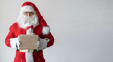 Santa Claus holds a box with a gift in his hands. It stands near the space for the text. Isolated on white.の写真素材