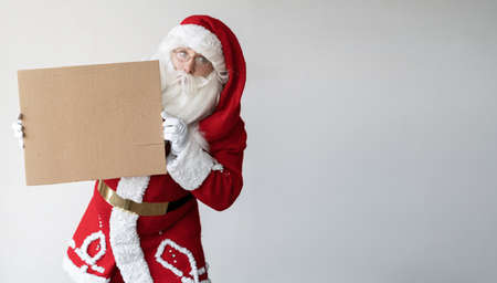 santa claus stands on a white background holding an empty sign in his hands. Copy space.の写真素材