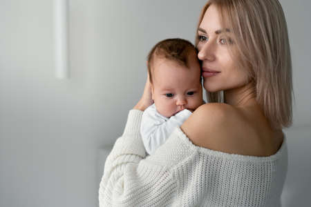 Mom is standing, holding and hugging her newborn baby. Her lips gently brush against his cheek. Place for text.の写真素材