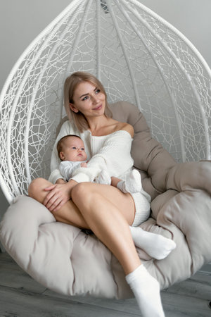 Mom and baby are sitting on a wicker chair. The woman hugs her daughter. Motherhood and childhood...