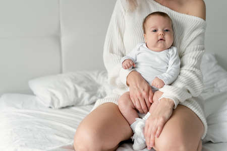 The baby is 4 months old in her mother's arms. The woman is kneeling on the bed. Childhood and family concept.の写真素材