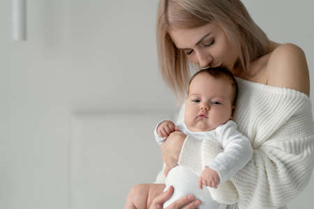 A woman with a newborn baby in her arms kisses her daughter's head. Clothes made of quality white cotton. Place for your text. Copy space.の写真素材