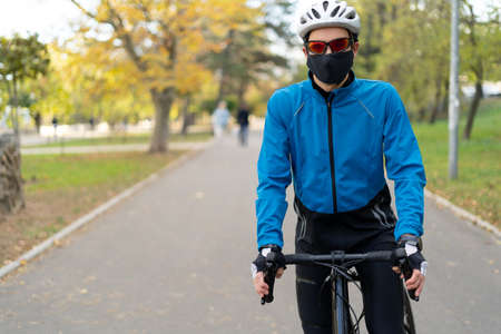 An athlete in glasses and a protective mask stands in the park on a bicycle road with a bicycle. Quarantined sports and outdoor recreation.の写真素材