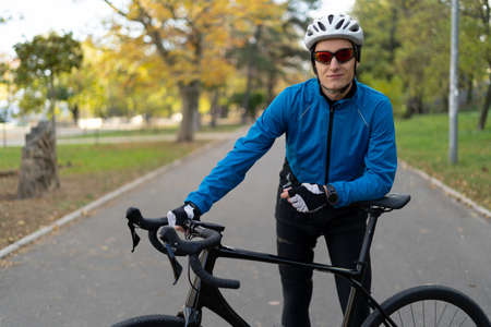 An athlete in glasses and a protective bicycle helmet stands in the park on a bicycle road. Sports and outdoor recreation. Copy space.の写真素材