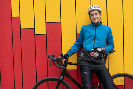 A young man in a helmet with a bicycle stands against a bright wall in the street. Sports that are held in the open air. Relaxation and healthy lifestyle. Copy space.の写真素材