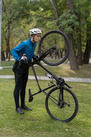 An athlete in the park holds a bicycle on one wheel. Sports that are held in the open air. Safety helmet and training suit. Copy space.の写真素材