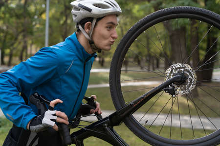 Close-up athlete in the park holds a bicycle on one wheel. Sports that are held in the open air. Safety helmet and training suit. Copy space.の写真素材