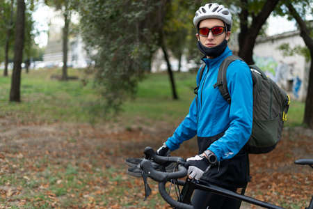 A man athlete stands in the park with a bicycle. He wears a mask and a protective helmet on his head. Sports activities in quarantine. Copy space.の写真素材