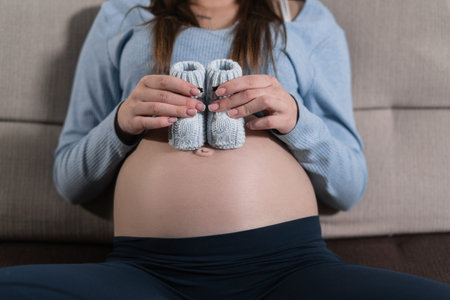 Close up of belly of a pregnant woman. two blue booties. The concept of waiting for a boy.