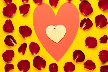 big red heart in it small made of wood in rose petals on yellow background. Copy space. Concept to celebrate valentines dayの写真素材