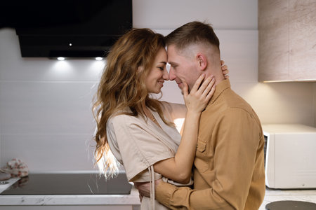 young caucasian couple kissing and chatting at home in the kitchen. The woman hugs the man tenderly.