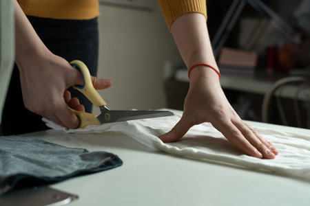 Womens hands cut fabric on a paper pattern with tailors scissors on a white table. A dressmaker at work in a sewing studio.の写真素材
