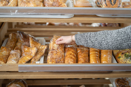 A womans hand takes a loaf from a wooden shelf with bread and baguettes in the supermarket. Products...