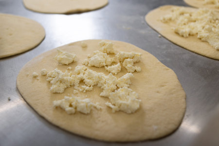 Dough circles for dumplings and pies are rolled out on a metal board, two mugs are filled with...