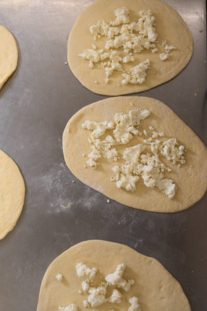 Circles of dough stuffed with cheese for dumplings and pies lie on a metal board. Raw dough and...