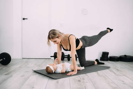 A young European mother with her little daughter on the floor is doing fitness and stretching. Exercise at home and restore health.の写真素材