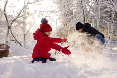 Dad of Caucasian ethnicity and his little daughter in a red jacket in winter throw snow in the park. Family and fun in the snow.の写真素材