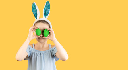 Happy Easter, kids. A girl in rabbit ears on her head holds two decorated eggs in her hands and...
