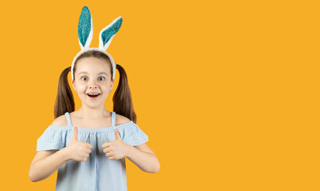 A little girl with bunny ears on her head raises two thumbs up and a smile on her face. Baner.