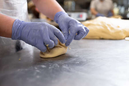The hands of the cook make pies with filling from yeast dough. Raw pastries on a metal board. Work in the confectionery shop.の写真素材