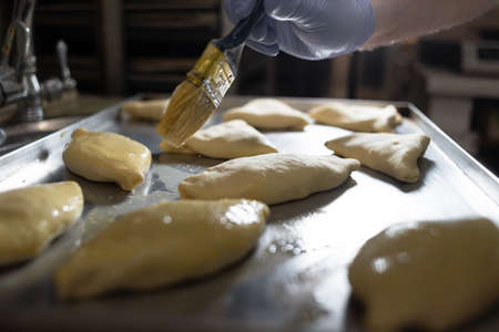 The cook greases small pies on a metal baking sheet with a brush and vegetable oil. Raw dough in the kitchen at the bakery. Flour products and products.の写真素材