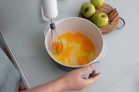 With an immersion blender with a whisk, the girl beats eggs in a ceramic frying pan. The process of making a dough for home baking. Cooking pie.の写真素材