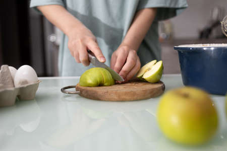 Close-up of the hand of a female chef who cuts apples for a pie in the home kitchen. Homemade baking process and ingredients for cookies, pies, fruit baskets.の写真素材