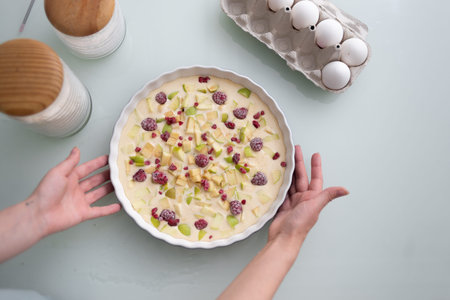 Raw summer sponge cake with berries, raspberries, apple and sugar dough for vegetarians. Summer food, summer cake in a ceramic baking dish and the hands of the chef.の写真素材