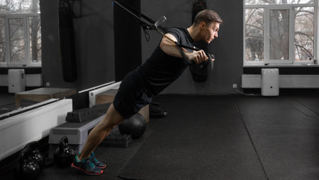 A fit man works out in the gym on the simulator, shakes the muscles of the arms and back, does...
