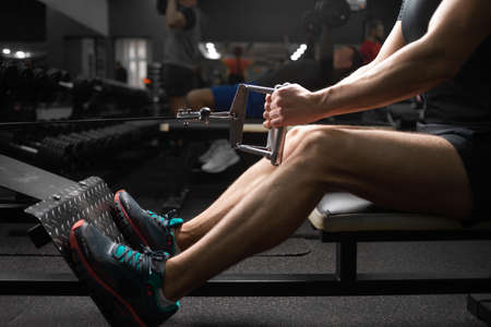 Close-up of the legs of a fit athletic man who trains in the gym on the simulator, shakes the muscles of the arms, performs exercises, a young athlete alone.の写真素材