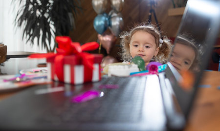 a red box stands near the laptop on the table, a lot of colored confetti. The girl looks at the...