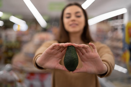 Young Caucasian lady in a supermarket buys an avocado. A woman buys groceries and basic goods at a...