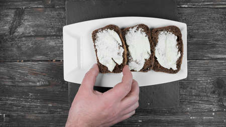 on a white plate Fresh homemade bread and a white spread on it a mans hand takes one slice. rustic background,の写真素材