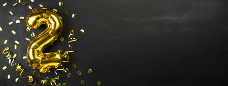 gold foil balloon number two or two, birthday greeting card with the inscription 2.black concrete background. Celebrating the anniversary. Banner. copy spaceの写真素材