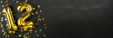 gold foil balloon number twelve. Birthday or anniversary greeting card with the inscription 12. black concrete background. Anniversary celebration. Banner. copy spaceの写真素材