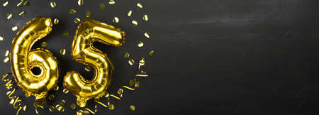 gold foil balloon number sixty-five. Birthday or anniversary card with the inscription 65. Black concrete background. Anniversary celebration. Banner. copy spaceの写真素材