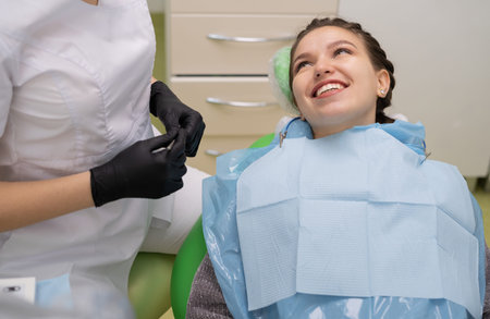 A patient with white teeth and a smile at the dentists appointment sits in a chair with a napkin on...