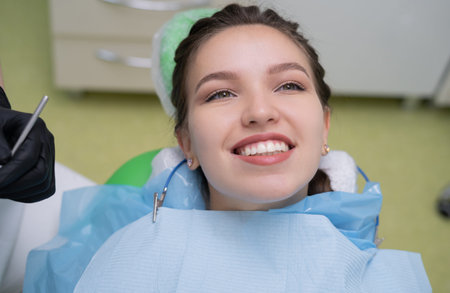 A portrait of a patient with white healthy teeth and a smile at the dentists office, she sits in a...