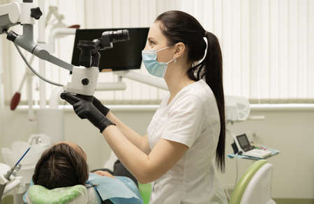 Female professional dentist doing various dental procedures and prosthetics to a patient in a modern office using a microscope.の写真素材